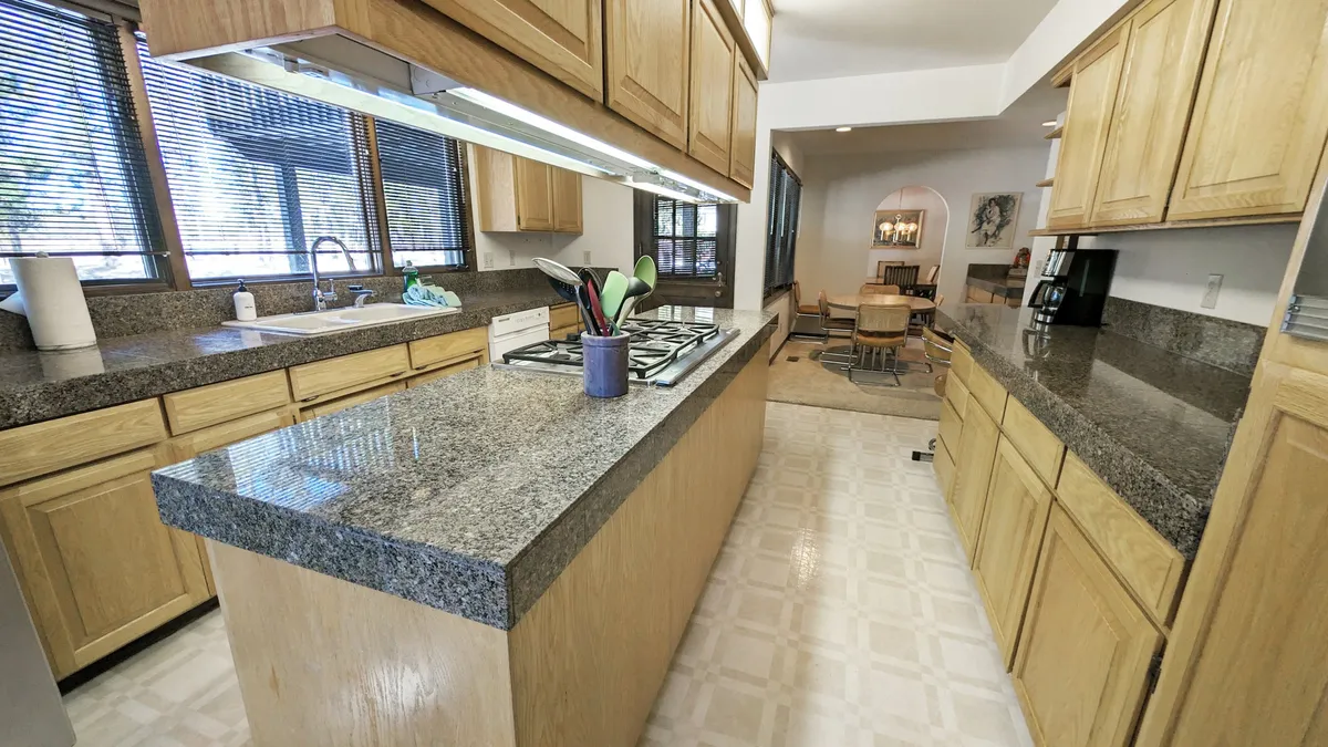 A welcoming chef’s kitchen with a large granite countertop, central kitchen island, gas stove, and wide window views. The layout is ideal for collaborative cooking and gathering, with abundant counter space for preparing meals or hosting snack spreads.