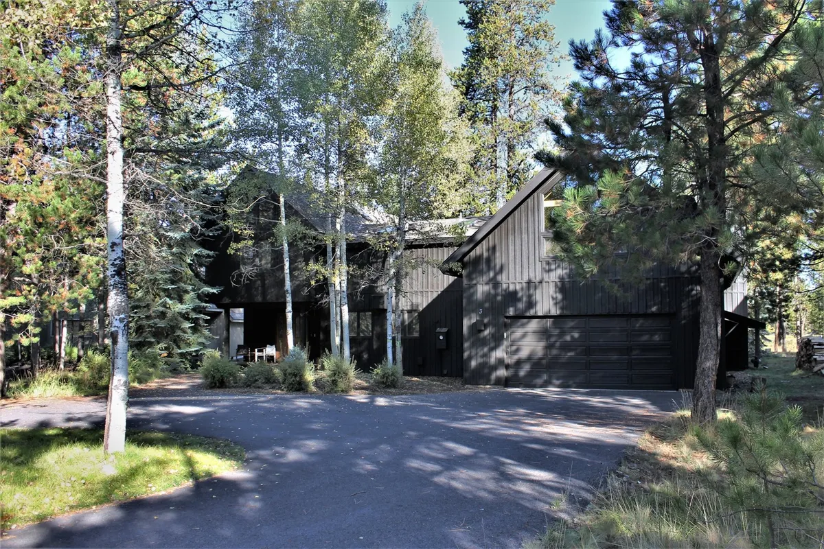 A modern black wooden exterior nestled among tall trees, with a driveway leading to the home. The tranquil outdoor scene emphasizes the peaceful surroundings and invites families to imagine outdoor barbecues or setting out on bike rides to resort amenities.