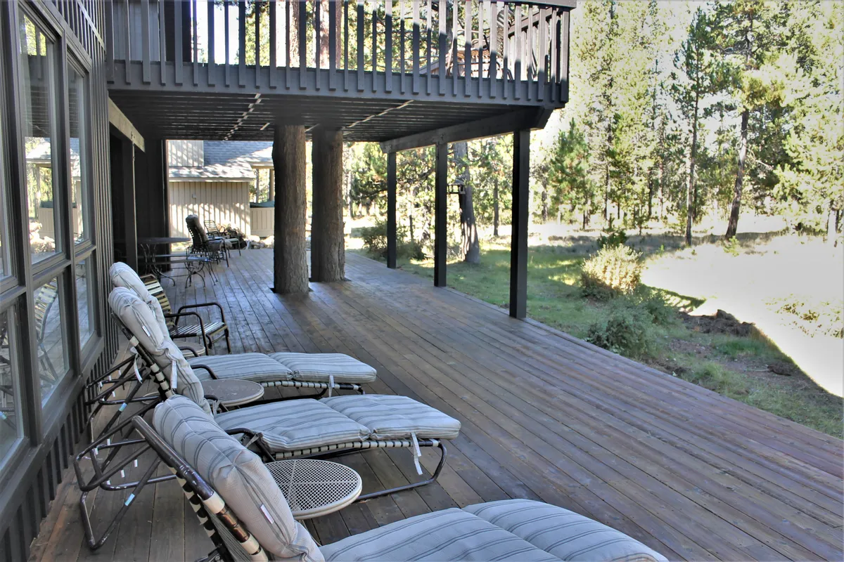 This image shows a peaceful wooden deck surrounded by towering trees, with comfortable deck chairs arranged for relaxation. The setting evokes a tranquil outdoor retreat, inviting guests to unwind and connect with nature just steps outside the home.