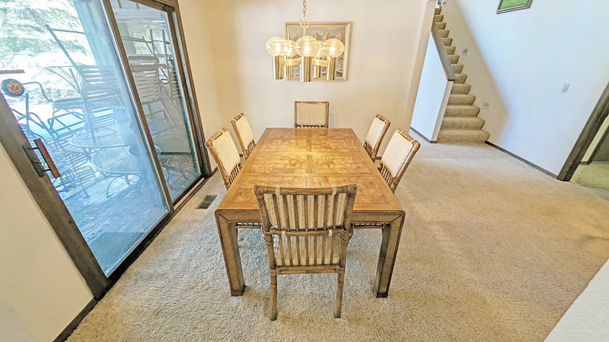 This image showcases a warm, inviting dining area with a wooden table, chandelier, and a sliding glass door that leads directly to a patio outside. The natural light streaming through the glass door hints at a seamless connection between indoor and outdoor spaces, suggesting easy access to the backyard or deck—an ideal spot for relaxing after outdoor adventures with pets.