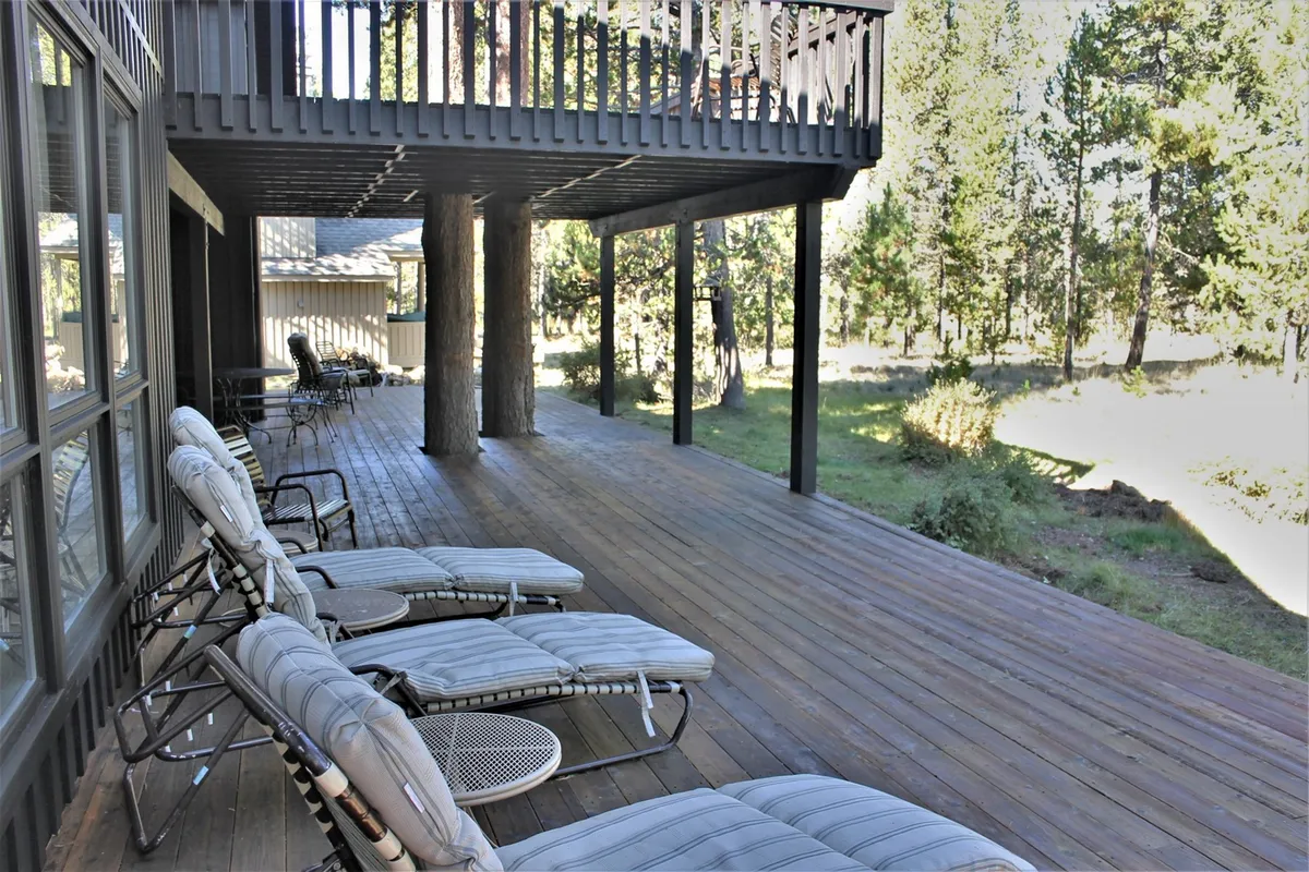This exterior shot features a spacious wooden deck with deck chairs, bordered by tall trees and tranquil greenery. The open-air layout emphasizes privacy and seamless connection to the outdoors.