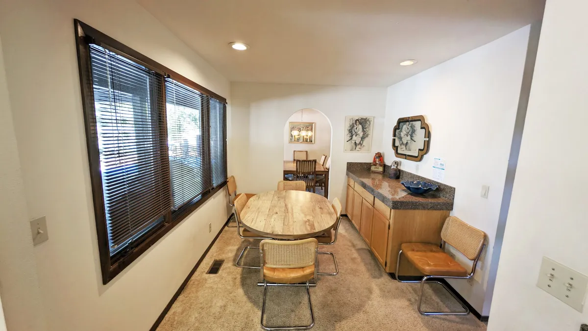 A dining area with a wooden table, large windows that frame views of the natural landscape, and decorative wall art. The space is bathed in natural light, suggesting an inviting spot for coffee or quiet moments while enjoying the view.
