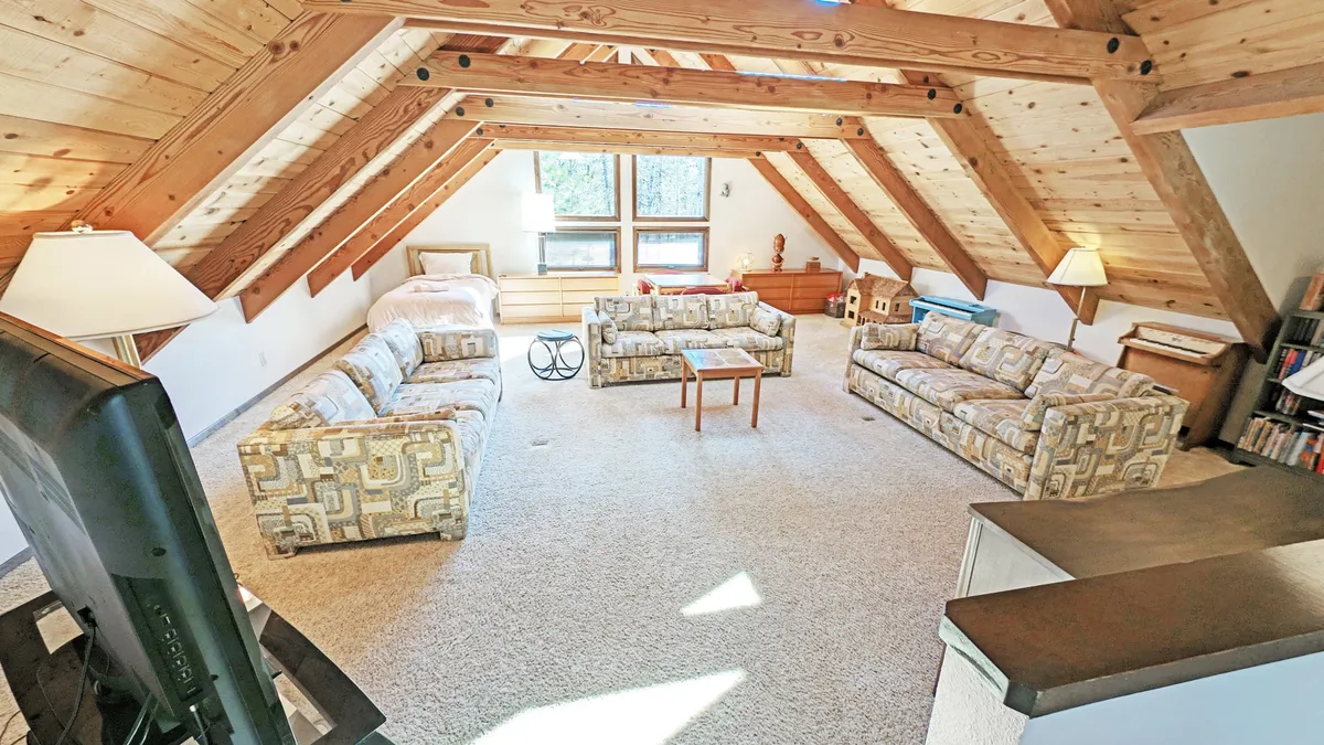 A cozy, relaxed living area with comfortable sofa seating arranged near large windows and wooden beams. Abundant natural light pours in, and the space feels open, inviting, and closely connected to the outdoors—ideal for pets to lounge in the sun after a day of outdoor activities.